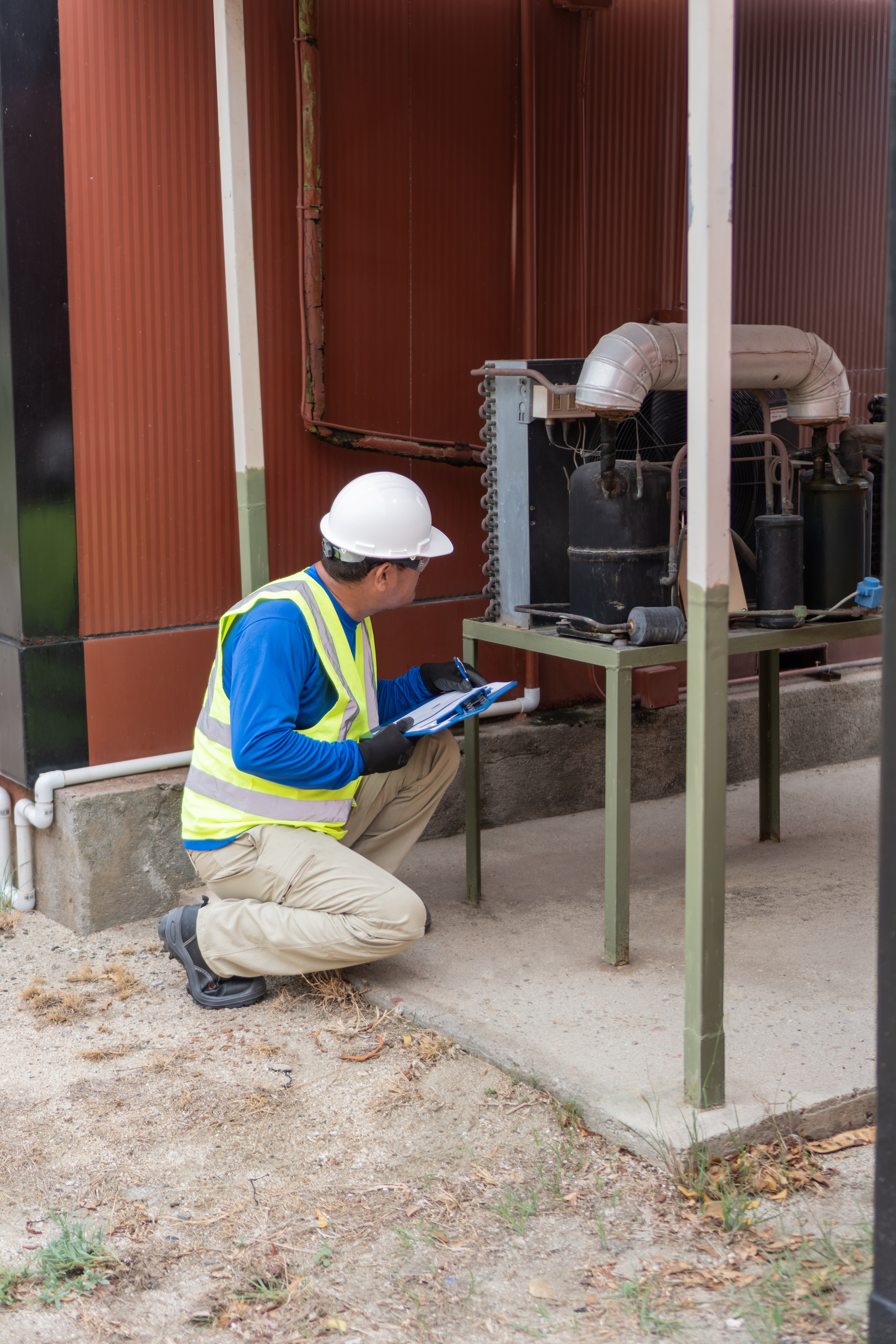 Technician in hard hat inspecting an outdoor industrial air conditioning unit
